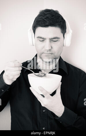 Uomo serio con cuffie wireless mangiare cereali per la prima colazione. Foto Stock