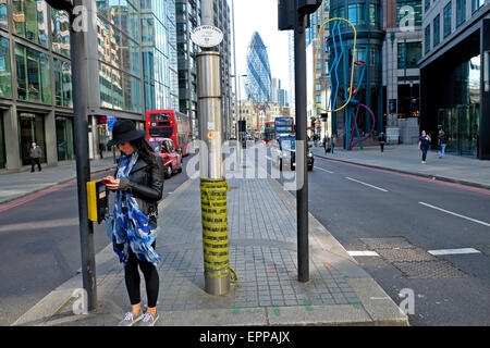 Un quartiere alla moda di giovane donna in piedi su Shoreditch High Street sms sul suo telefono cellulare al semaforo con una vista del gherkin edificio nella città di Londra UK KATHY DEWITT Foto Stock