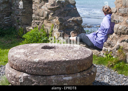 Donna seduta in resti di Old Mill, Melin Trefin, guardando verso il mare a Trefin o Trevine al Pembrokeshire Coast National Park, Galles, Regno Unito a maggio Foto Stock