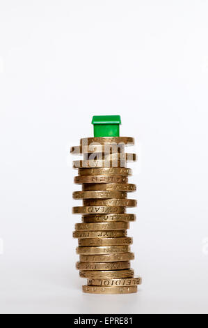 Un piccolo modello di plastica casa verde sulla cima di un palo di libbra di monete. Finanziamento di alloggi concetto. Foto Stock