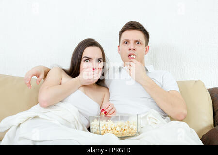 Frightened giovane coppia attraente comodamente seduto sul divano nel soggiorno di casa coperte con coperta e guardare scary horror sulla te Foto Stock