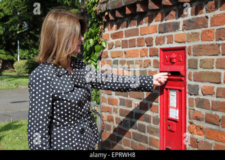 La donna ha appena pubblicato la lettera in rosso postbox nel muro di mattoni in Inghilterra, Regno Unito Foto Stock