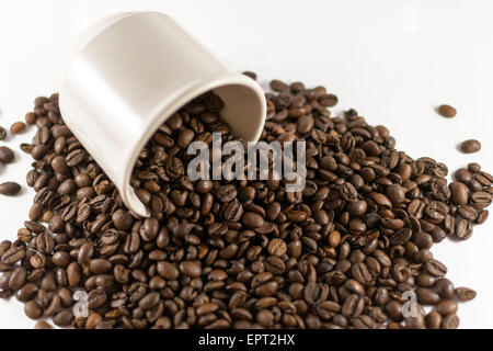 Primo piano di molti chicchi di caffè la fuoriuscita di una tazza su bianco Foto Stock