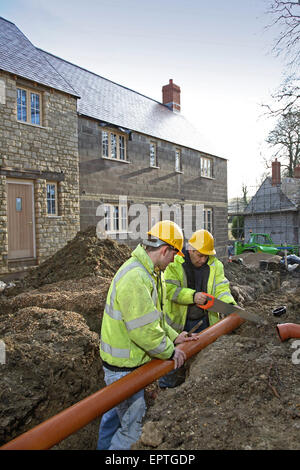 Lavoratori edili il taglio di tubi per il drenaggio di installazione su un piccolo, alloggi rurali lo sviluppo in Dorset, Regno Unito Foto Stock