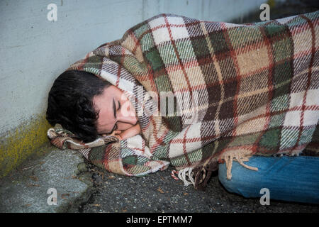 Giovane maschio mendicante che dorme sul marciapiede della città con coperta sulle spalle Foto Stock