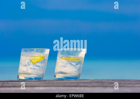 Bicchieri di acque con il limone su legno su sfondo del mare Foto Stock