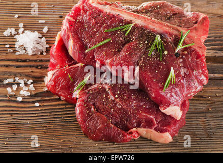 Bistecca di manzo con il condimento e erbe aromatiche fresche sulla tavola di legno. Messa a fuoco selettiva Foto Stock