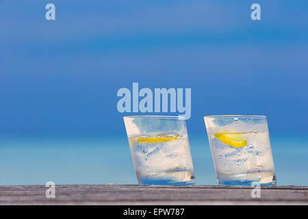 Bicchieri di acque con il limone su legno su sfondo del mare Foto Stock