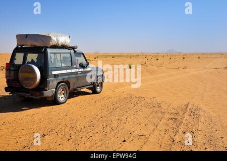 Veicolo fuoristrada con una tenda del tetto sul lato sporco della pista, Aicha monolito dietro, regione di Adrar, Mauritania Foto Stock