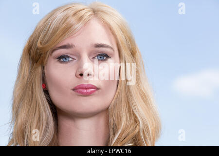 Faccia il ritratto di una giovane donna con dei bellissimi occhi azzurri e lunghi capelli biondi contro un cielo blu con copyspace Foto Stock