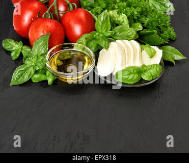 Insalata Caprese ingredienti. Basilico fresco, pomodoro, mozzarella e olio di oliva su sfondo nero Foto Stock