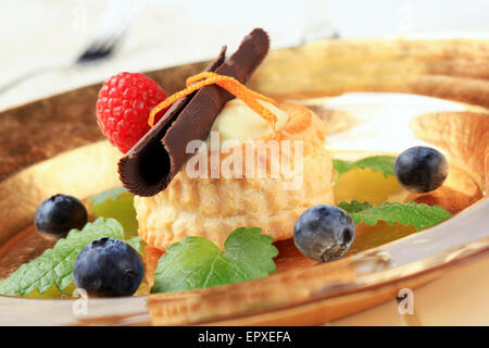 Crema di latte riempito vol-au-vent guarnita con ricciolo di cioccolato e frutta Foto Stock