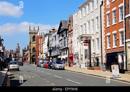 Edifici e negozi lungo Bridge Street con San Pietro e la chiesa di St Michaels chiesa alla parte posteriore di Chester, Cheshire, Inghilterra, Regno Unito Foto Stock