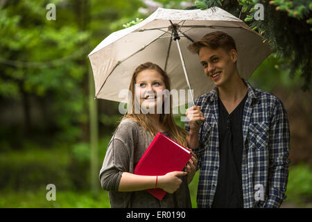 Coppia giovane nel parco sotto un ombrello, una ragazza tiene un libro rosso nelle sue mani. Foto Stock