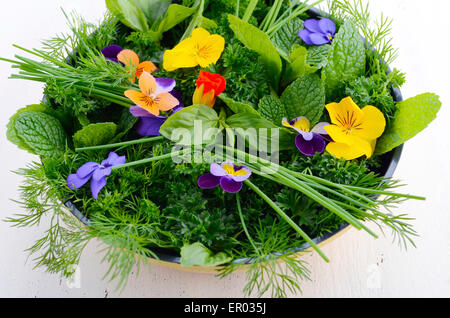 La cucina con le erbe concetto con erbe aromatiche e fiori commestibili in giallo moderno padella padella bianco sul tavolo di legno. Foto Stock