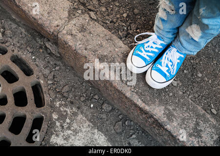 Adolescente in piedi in jeans e scarpe blu sostare sul bordo della strada. Foto con messa a fuoco selettiva e DOF poco profondo Foto Stock