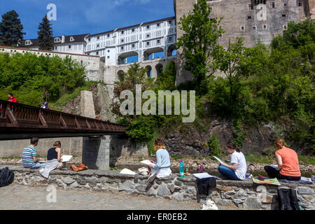 Il centro storico di Cesky Krumlov, Boemia, Repubblica Ceca, UNESCO, i turisti sono seduti sulla sponda del fiume e trascina in un taccuino Foto Stock