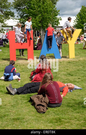 Hay Festival Powys, Wales, Regno Unito Maggio 2015 bambini giocare sul gigante segno di fieno sui prati del Festival come visitatori adulti sedersi e rilassarsi. Foto Stock