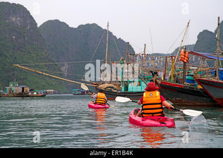 Il kayak passato barca da pesca in Cua Van, il più grande villaggio galleggiante nella baia di Halong Foto Stock