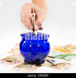 La mano viene messa valuta euro nota nella casella di denaro (piggy). Valuta Euro è visibile sotto piggy come bene. Foto Stock