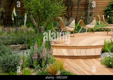 Curva decking in legno e sedie circondati da confini nella Royal Bank of Canada giardino al Chelsea Flower Show. Foto Stock