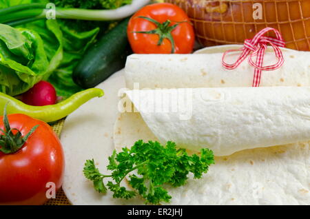 Svuotare tortillas legate con un nastro rosso su un tavolo con il pomodoro, la lattuga e prosciutto Foto Stock