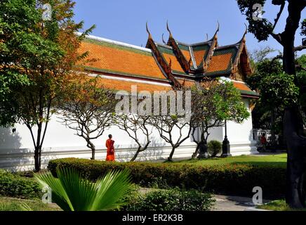 Bangkok, Thailandia: monaco buddista nel tradizionale tunica arancione passeggiate nei giardini accanto a un padiglione di Wat Suthat Foto Stock