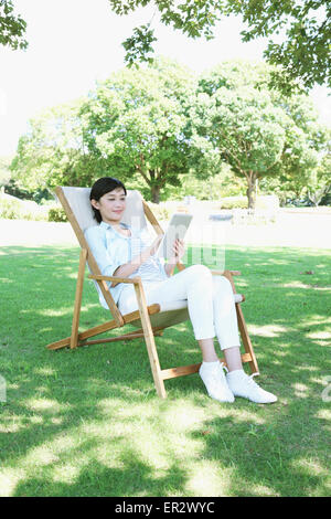 Donna giapponese con la compressa sulla sedia a sdraio in un parco della città Foto Stock