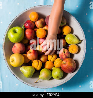 La mano di raggiungere per un frutto in una ciotola, sfondo blu Foto Stock