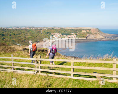 Coppia matura sul modo di Cleveland sentiero costiero con Runswick Bay Village in distanza. North Yorkshire, Inghilterra, Regno Unito Foto Stock