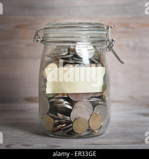 Monete in denaro di vetro vaso con etichetta vuota, concetto finanziario. Vintage sfondo di legno con luce drammatica. Foto Stock