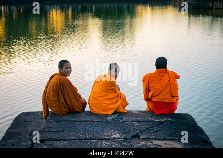 SIEM REAP, Cambogia - 30 ottobre 2014: il Principiante i monaci buddisti in arancione vesti sedersi sul bordo del fossato a Angkor Wat. Foto Stock