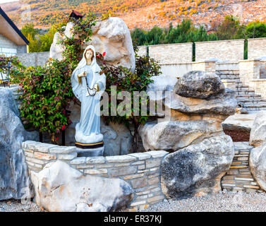 Statua della Vergine Maria con la preghiera in legno collana di perle in una casa giardino roccioso con treesin Medjugorje Foto Stock