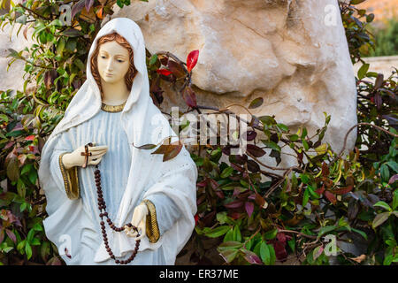 Statua della Vergine Maria con la preghiera in legno collana di perle in una casa giardino roccioso con treesin Medjugorje Foto Stock