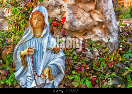 Statua della Vergine Maria con la preghiera in legno collana di perle in una casa giardino roccioso con treesin Medjugorje Foto Stock