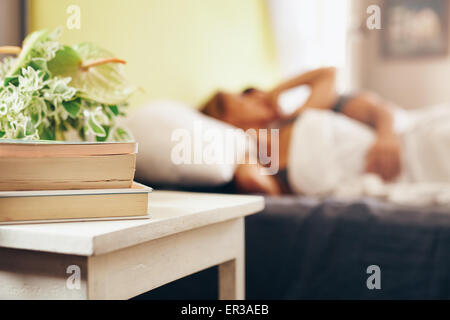 Tavolino con libri e fiori dal letto in camera da letto. Giovane dormire tranquillamente sul letto. Foto Stock