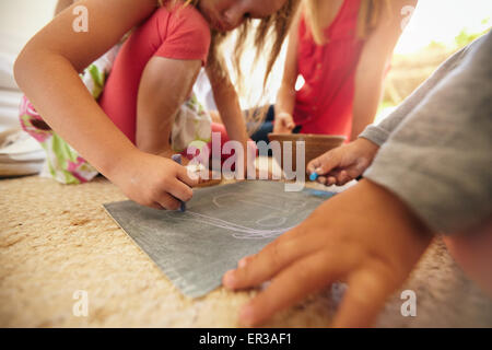 Bambina disegno con suo fratello e i genitori seduti a. Concentrarsi sulle ragazze mani di disegno con colori di gesso. Foto Stock