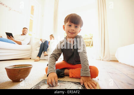 Carino piccolo ragazzo il disegno e la colorazione con suo padre e sua madre seduta sul divano con tavoletta digitale. Ragazzo seduto sul pavimento looki Foto Stock