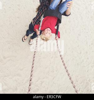 Vista in elevazione di una donna spingendo il suo figlio su uno swing Foto Stock