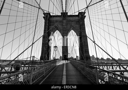 Silhouette di persone sconosciute attraversando a piedi il Ponte di Brooklyn come il sole sorge sopra gli archi a est - bianco e nero. Foto Stock