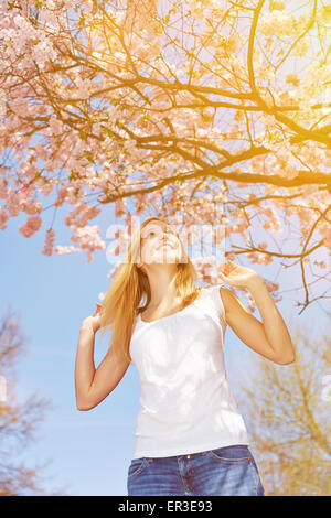 Felice ragazza entusiasta di Sun e la fioritura dei ciliegi in Primavera Foto Stock