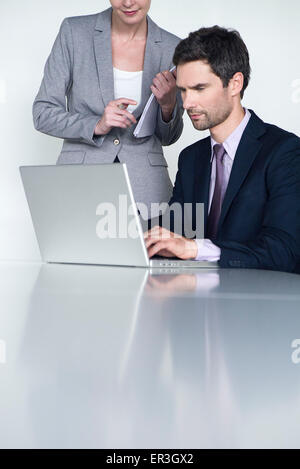 Imprenditore lavora su computer portatile, collega guardando sopra la sua spalla Foto Stock