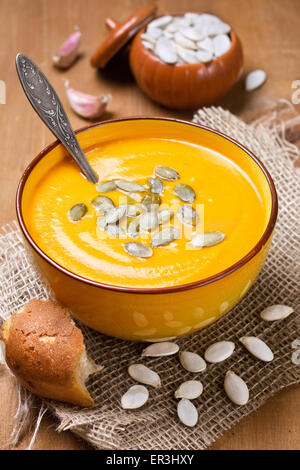 Zuppa di zucca - purea con i semi di zucca in una ciotola di colore giallo su uno sfondo di legno Foto Stock