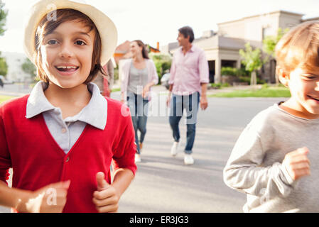 Ragazzi in esecuzione in street, famiglia camminando dietro di loro Foto Stock