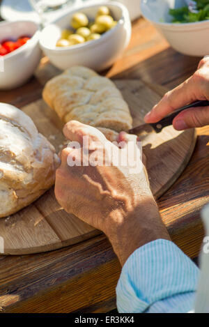 L'uomo le mani fresche di taglio della pagnotta di pane all'aperto Foto Stock