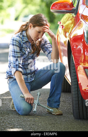 Frustrati Driver femmina con ferro di pneumatico cercando di cambiare la ruota Foto Stock