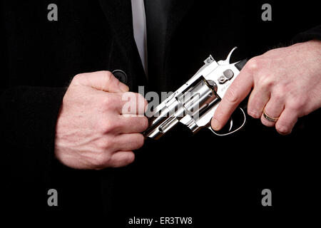 L'uomo prendendo revolver fuori del suo nero nella tasca del cappotto Foto Stock