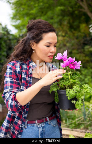 Giovane donna odore di una pianta in giardino Foto Stock