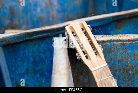 Vecchia chitarra indesiderati gettato in un metallo arrugginito cassonetto Foto Stock