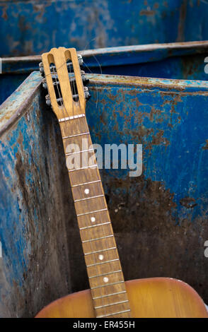 Vecchia chitarra indesiderati gettato in un metallo arrugginito cassonetto Foto Stock